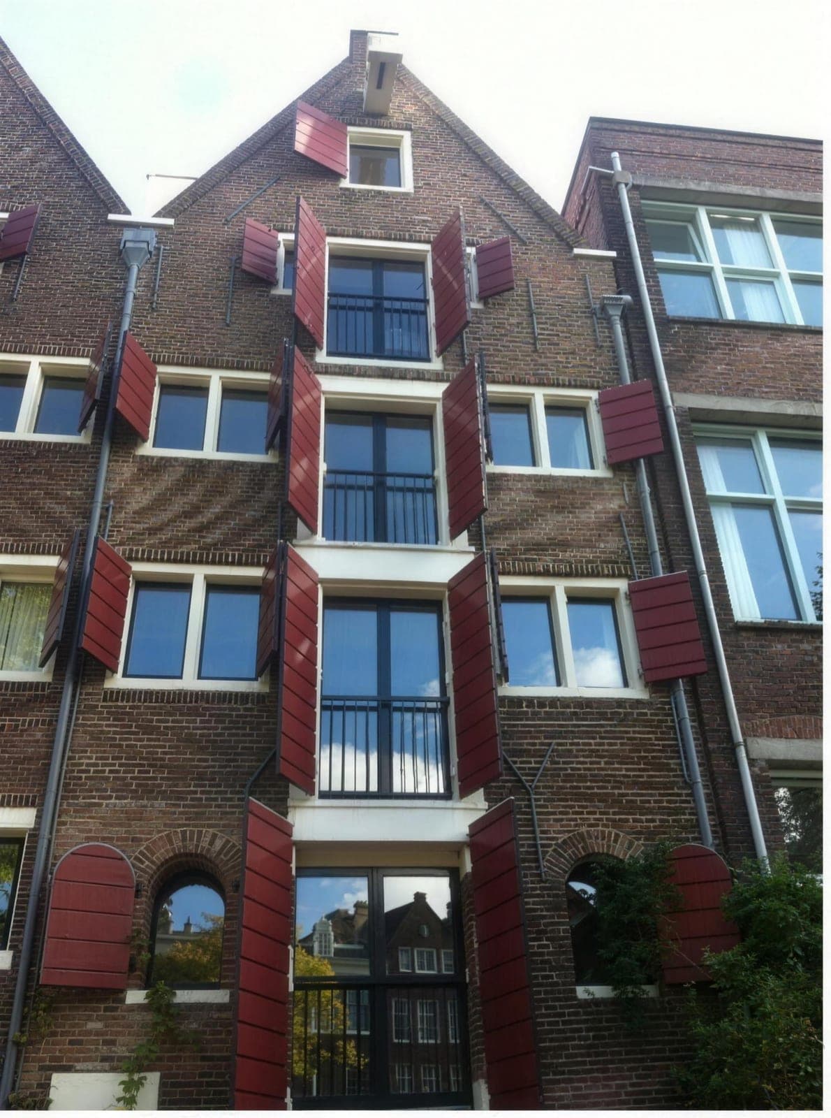 Gerenoveerde bakstenen gevel met rode luiken van een pand in Amsterdam